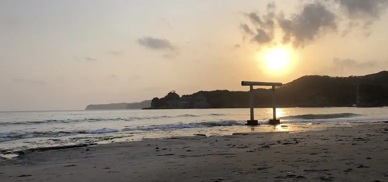 Zachód słońca nad spokojnym morzem, z bramą torii na plaży w Japonii.