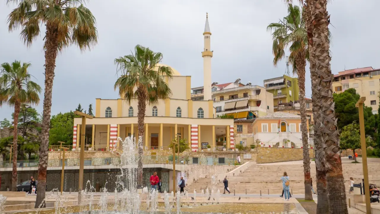 Plac z fontannami i palmami przed meczetem w Durrës, Albania. Ludzie spacerują po schodach.
