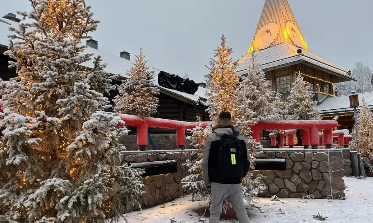 Ośnieżone choinki i budynek z wieżą w Rovaniemi, gdzie mieszka mikołaj. Mężczyzna z plecakiem stoi tyłem.