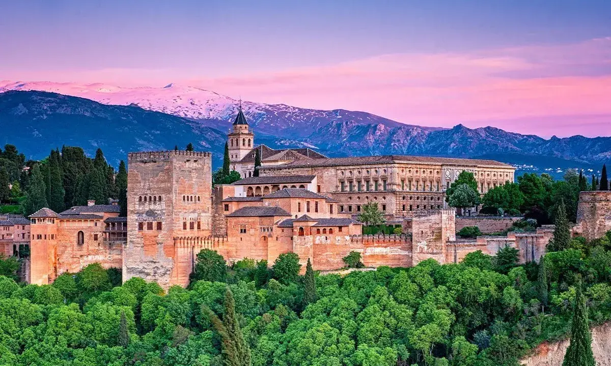 Alhambra w Granadzie na tle ośnieżonych gór i różowego nieba o zachodzie słońca.