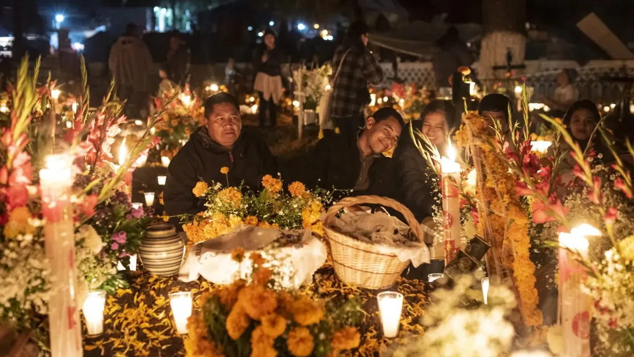 Rodzina przy grobie ozdobionym świecami i kwiatami na Dia de los Muertos.