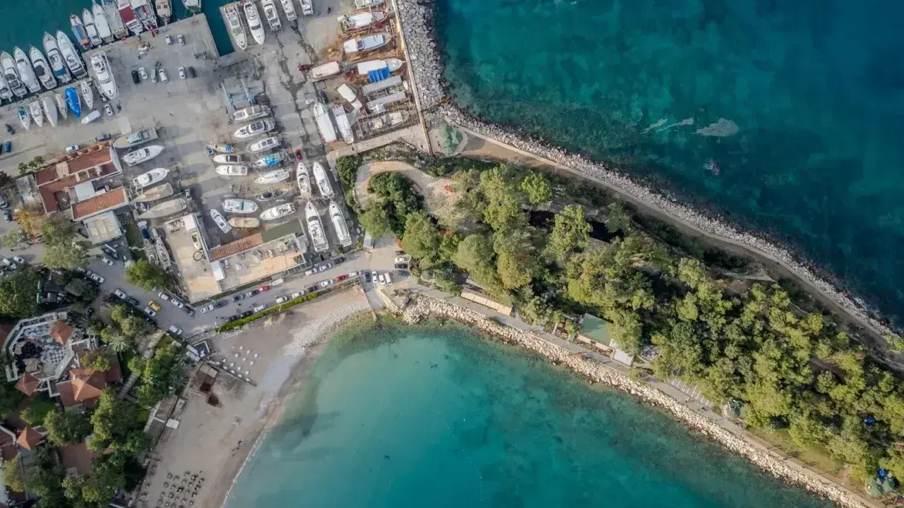 Widok z lotu ptaka na port i plażę w Kemerze. Widać liczne jachty i łodzie, a także zielony teren z drzewami. To idealne miejsce na odkrywanie atrakcji Kemer Turcja.