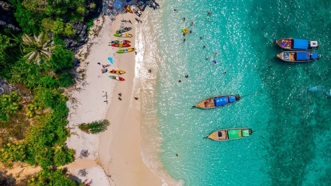 Rajska plaża na tajlandzkiej wyspie Phuket. Kajaki czekają na plaży, a turyści kąpią się w turkusowej wodzie.