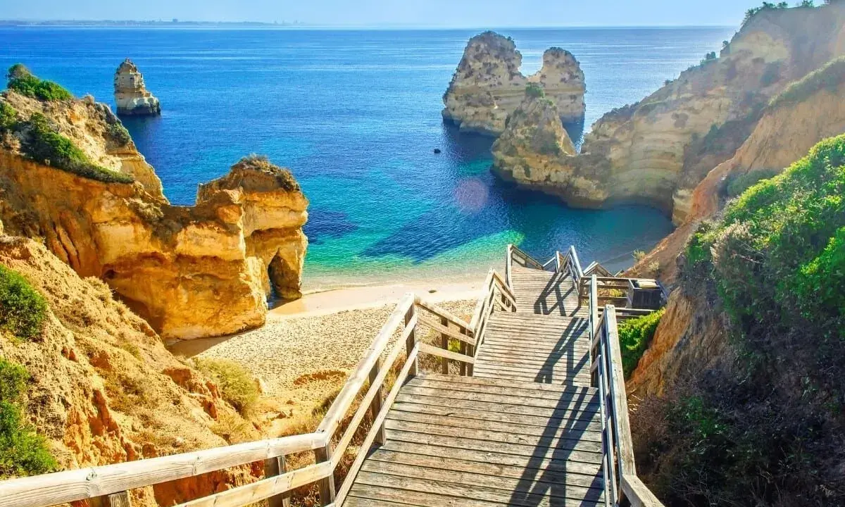 Schody prowadzą na piaszczystą plażę z turkusową wodą i skalnymi formacjami. To idealne miejsce, by zobaczyć, co Portugalia ma do zaoferowania.