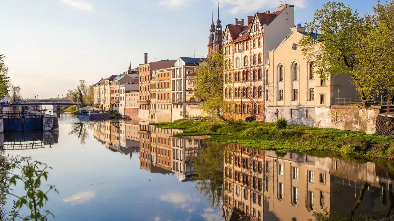 Nad rzeką w Opolu, w blasku słońca, odbijają się kamienice. To jedne z wielu magicznych miejsc opolskich, które zachwycają spokojem i pięknem.