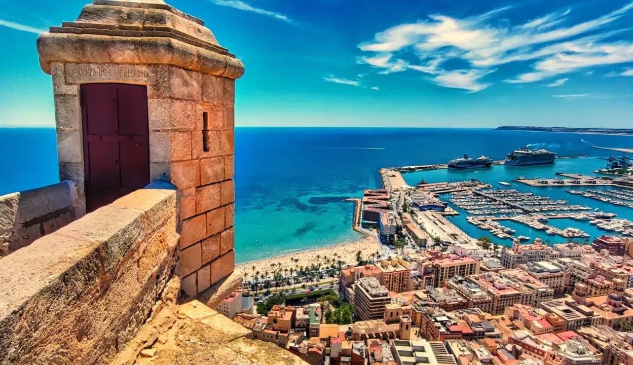 Alicante co zobaczyć: widok z zamku na port, plażę i miasto. W oddali statki wycieczkowe.