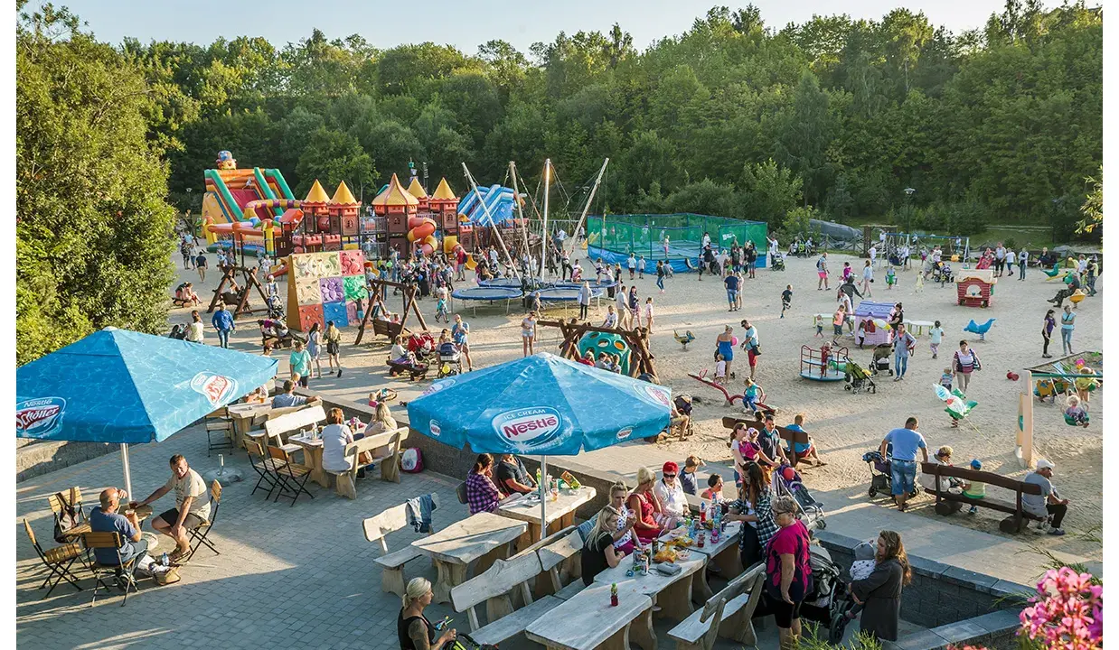 Rodzinna zabawa na placu zabaw w Ocean Park Władysławowo. Dzieci szaleją na dmuchanych zamkach, trampolinach i zjeżdżalniach, podczas gdy dorośli odpoczywają przy stolikach.