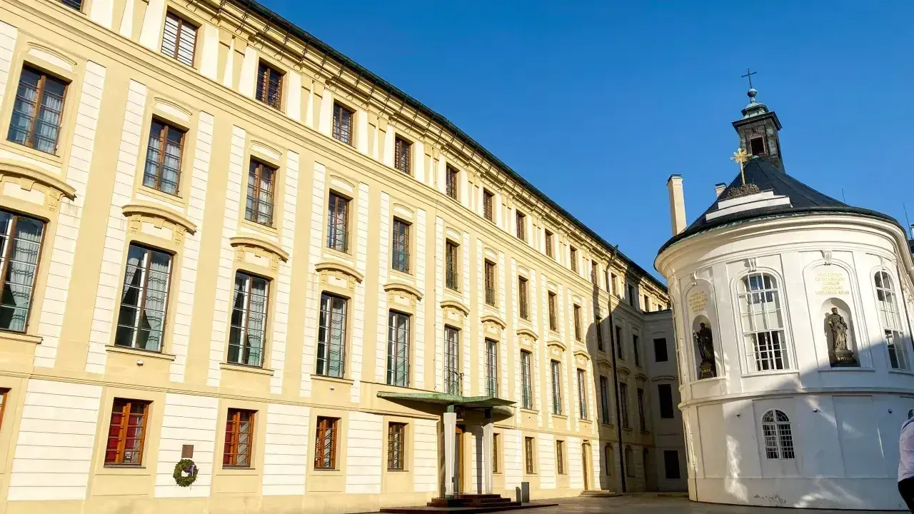 Zamek na Hradczanach, z jego długą, kremową fasadą i okrągłą, białą kaplicą, prezentuje się majestatycznie pod błękitnym niebem.