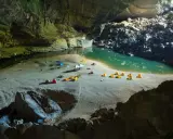 Obóz w jaskini Son Doong: namioty rozbite na piaszczystej plaży nad turkusową wodą, otoczone skalnymi ścianami.