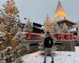 Ośnieżone choinki i budynek z wieżą w Rovaniemi, gdzie mieszka mikołaj. Mężczyzna z plecakiem stoi tyłem.