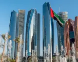Nowoczesne wieżowce w Abu Zabi, flaga Zjednoczonych Emiratów Arabskich powiewa na wietrze, fontanny i palmy tworzą malowniczy widok.