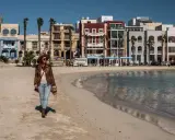 Kobieta spaceruje po piaszczystej plaży w pretty bay Malta, w tle kolorowe budynki i palmy.