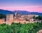 Alhambra w Granadzie na tle ośnieżonych gór i różowego nieba o zachodzie słońca.