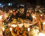 Rodzina przy grobie ozdobionym świecami i kwiatami na Dia de los Muertos.