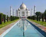 Majestatyczny Taj Mahal w Indiach odbija się w spokojnej wodzie, otoczony zielonymi ogrodami i strzelistymi cyprysami.