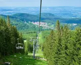 Kolejka linowa w Górach Izerskich, w kierunku najwyższego szczytu. Widok na las i zabudowania.