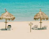 Idealna pogoda Tunezja wrzesień: dwa słomiane parasole i leżaki na piaszczystej plaży, turkusowe morze w tle.