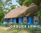 Niebieski dom z strzechą i zielonym płotem w skansenie.