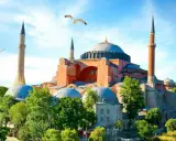Majestatyczna Hagia Sophia w Stambule, otoczona zielenią, z mewami szybującymi na błękitnym niebie.