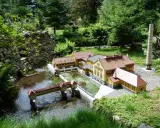 Miniaturowa zabudowa z mostkiem i rzeką, jak w parkach miniatur w Polsce.