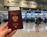 Polski paszport i bilet lotniczy w ręku, w tle tablica "THAILAND BANGKOK" i stanowiska "Visa on Arrival". Sprawdzanie tajlandia warunki wjazdu.