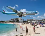 Samolot Airfly.com przelatuje nisko nad plażą pełną turystów, którzy obserwują jego lądowanie.