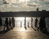 Ludzie spacerują i łowią ryby na promenadzie nad morzem. Słońce odbija się w wodzie, tworząc złoty blask.
