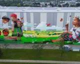 Kolorowe murale w Polsce: dzieci w strojach ludowych zbierają jabłka na tle sielskiego krajobrazu, dziewczynka z psem dmucha dmuchawiec.