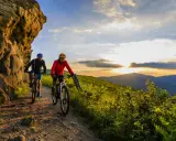 Dwóch rowerzystów na górskim szlaku, odkrywających najlepsze trasy rowerowe w Polsce o zachodzie słońca.