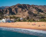 Słoneczne gran canaria plaże z piaszczystym brzegiem, turkusową wodą i górami w tle. Ludzie odpoczywają pod parasolami.