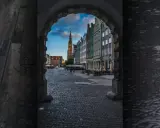 Deszczowe popołudnie w Gdańsku. Widok na Długi Targ przez bramę, kolorowe kamienice i wieżę Ratusza.