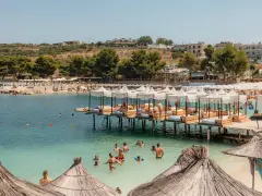 Słoneczny dzień w Ksamil Albania. Ludzie relaksują się na plaży i w wodzie, a nad zatoką unoszą się białe parasole.