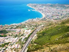 Widok z góry na wybrzeże Costa del Sol, z błękitnym morzem, plażą, miastem i zielonymi wzgórzami.