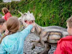 Dzieci w parku rozrywki Zatorland dotykają paszczy dinozaura.