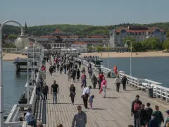 Tłum ludzi spaceruje po molo, podziwiając nadmorskie widoki. To popularne gdańsk atrakcje, idealne na słoneczny dzień.