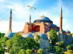 Majestatyczna Hagia Sophia w Stambule, otoczona zielenią, z mewami szybującymi na błękitnym niebie.