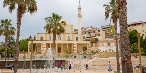 Plac z fontannami i palmami przed meczetem w Durrës, Albania. Ludzie spacerują po schodach.