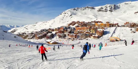 Ośrodek narciarski we francuskich Alpach. Tłumy narciarzy i snowboardzistów na stoku, w tle zabudowania. Francja narty gdzie najlepiej? Tutaj!
