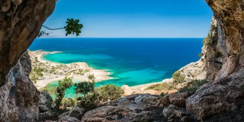 Widok z jaskini na turkusowe morze i plażę. Idealna kreta pogoda w kwietniu, słońce i błękitne niebo.