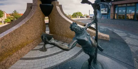 Rzeźba przed budynkiem, z czarną kulą i postacią trzymającą kielich. Zielona Góra atrakcje oferuje unikalne dzieła sztuki.