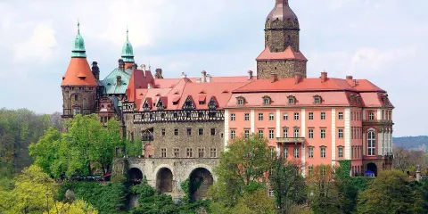Malownicze zamki i pałace wokół Wrocławia, jak ten imponujący kompleks z wieżami i czerwonymi dachami, zachwycają architekturą i otoczeniem.