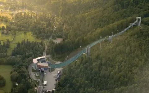 Skocznia narciarska w Wiśle, zielona latem, to jedna z głównych atrakcji regionu. Widać ją z lotu ptaka, otoczoną lasami.