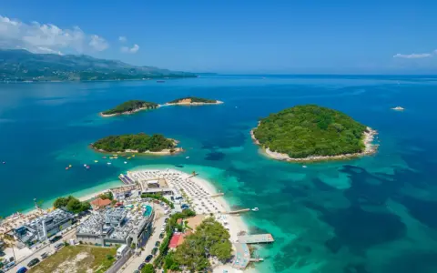 Malownicze wyspy otoczone turkusowym morzem, z piaszczystą plażą i nowoczesnymi budynkami. To raj na ziemi: Albania, plaża Ksamil.