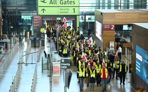 Tłum pracowników w kamizelkach odblaskowych z flagami maszeruje przez lotnisko w Berlinie, protestując. Strajk lotnisko Berlin zakłóca ruch.