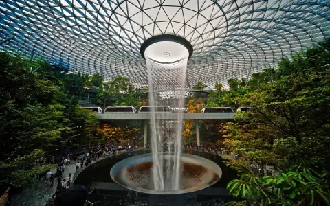 Wodospad HSBC Rain Vortex w porcie lotniczym Singapur-Changi, otoczony bujną zielenią i przejeżdżającymi pociągami.