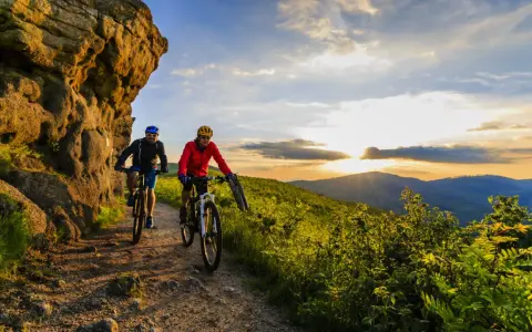 Dwóch rowerzystów na górskim szlaku, odkrywających najlepsze trasy rowerowe w Polsce o zachodzie słońca.
