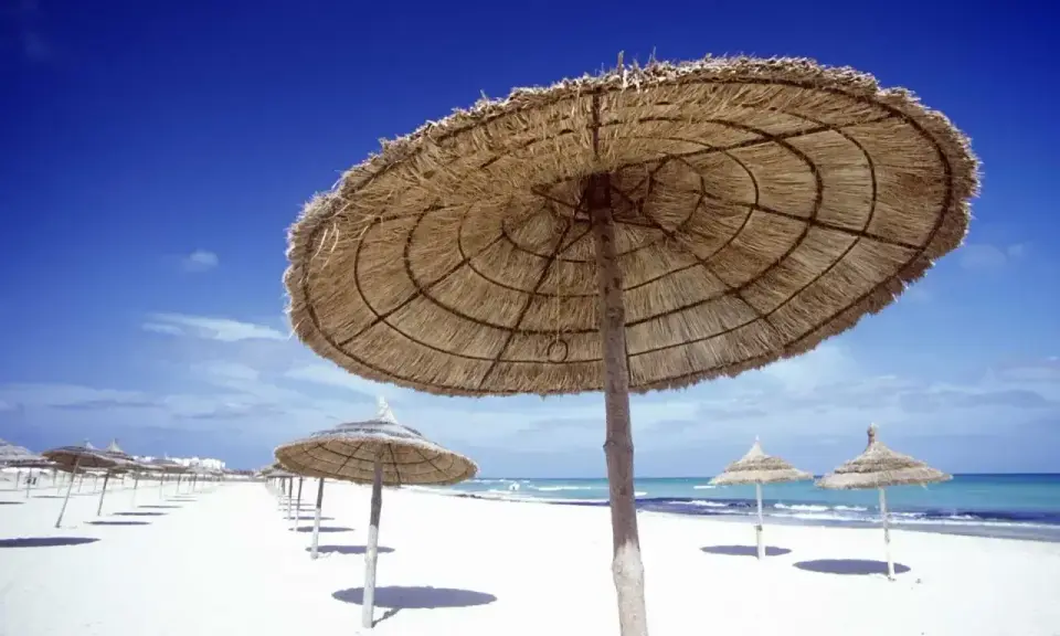Słomiane parasole na białej plaży, idealne na upalną tunezyjską pogodę w sierpniu. Błękitne niebo i morze.