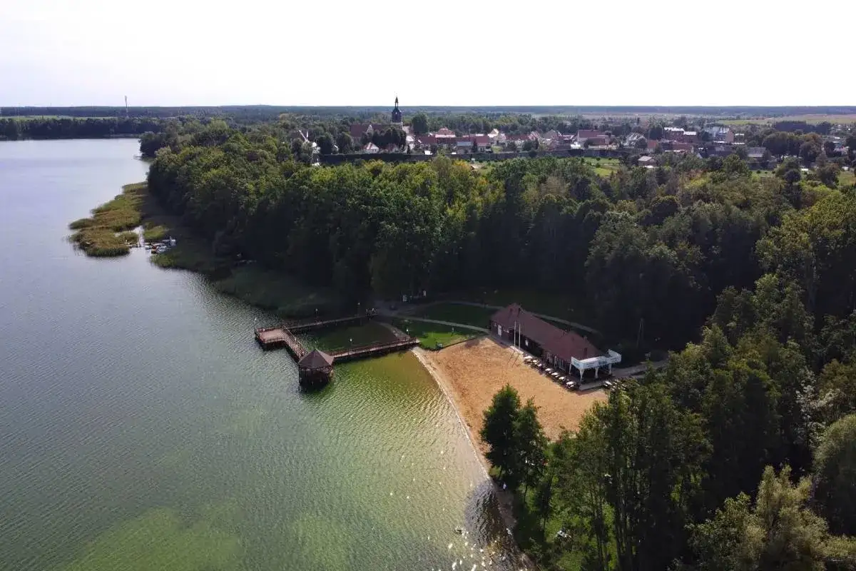 Malownicze pomorze zachodnie miejscowości nad jeziorem, z piaszczystą plażą, pomostem i budynkiem z tarasem.