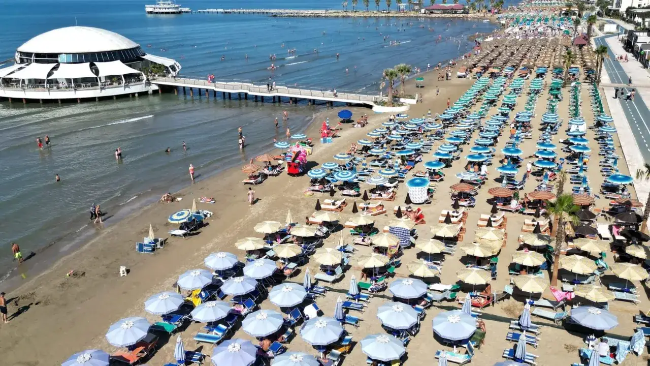 Słoneczna plaża w Durrës w Albanii, pełna leżaków i parasoli. W wodzie kąpią się ludzie, a na brzegu widać spacerujących.