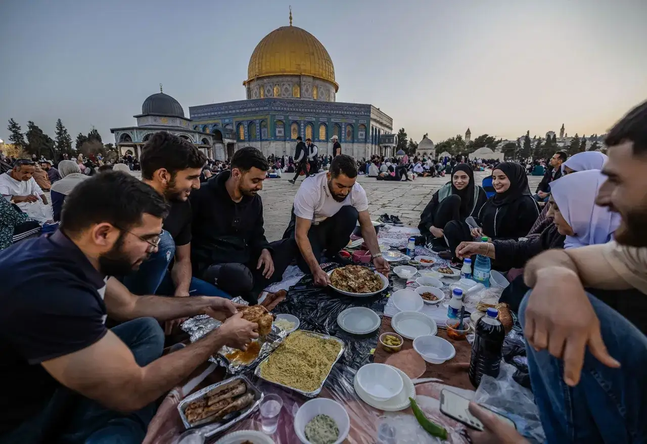 Rodzina i przyjaciele jedzą posiłek iftar na placu przed Kopułą na Skale. To pokazuje, czym jest ramadan.